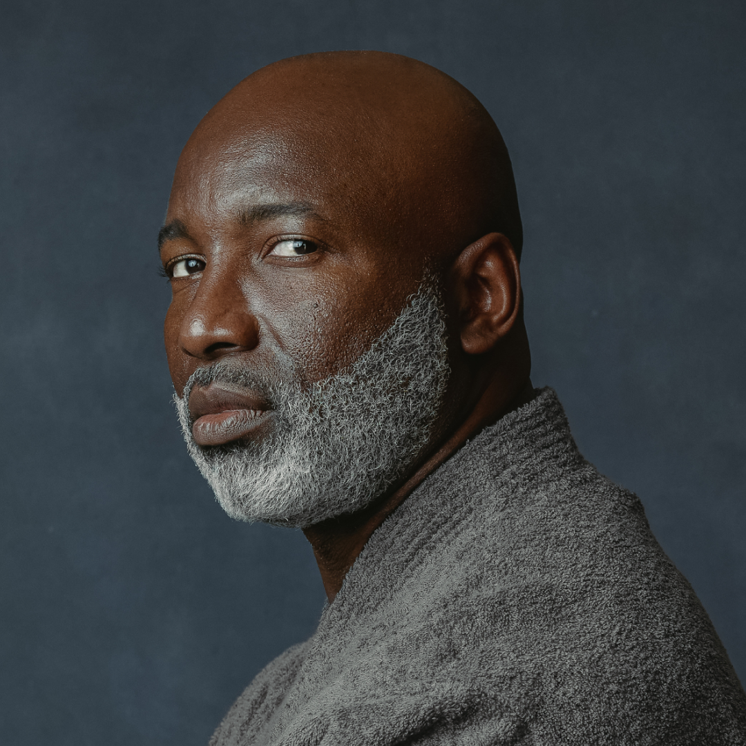 Man with a gray beard and gray sweater against a dark background