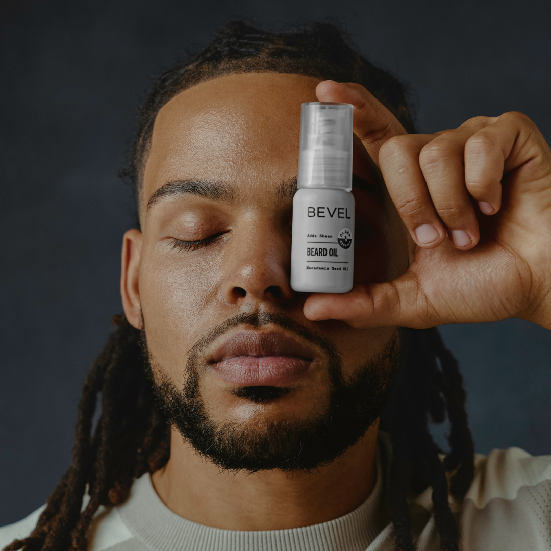 Man holding a BEVEL beard oil bottle near his face against a dark background