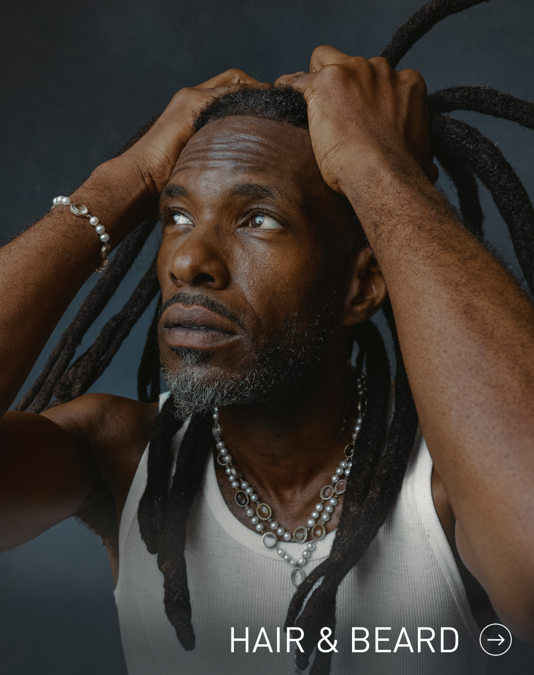 Man with dreadlocks adjusting his hair against a dark background