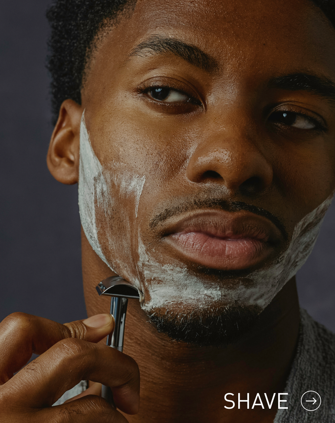 Man shaving with a razor and shaving cream on a dark background