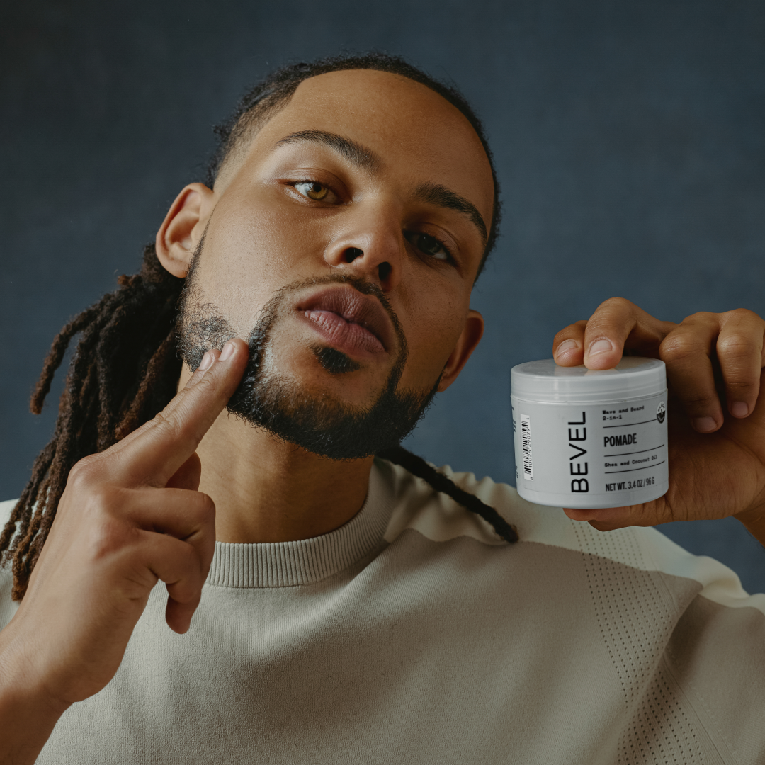 Man pointing to his beard holding a BEVEL pomade jar against a dark background