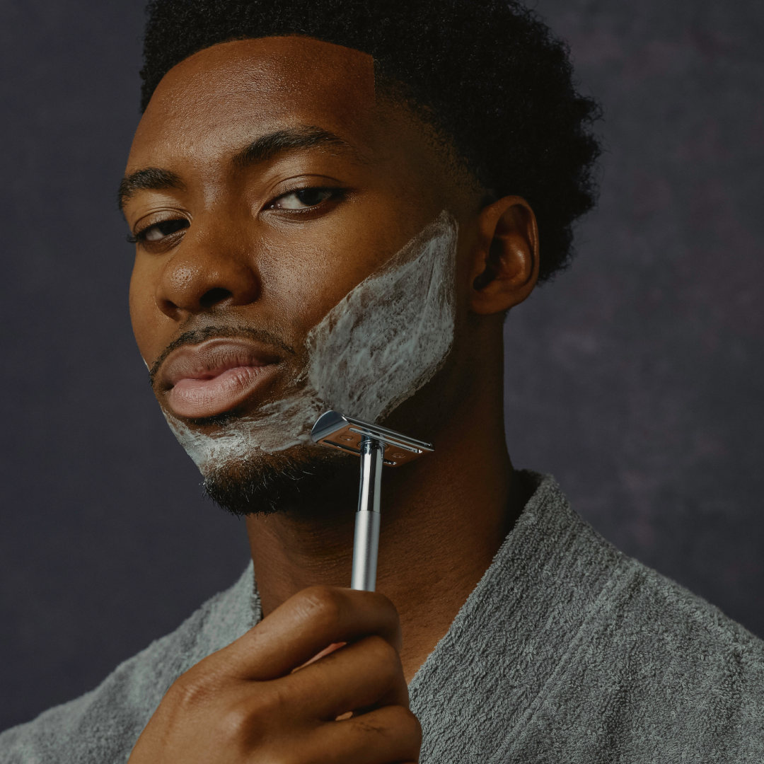 Man shaving his face with a razor against a dark background