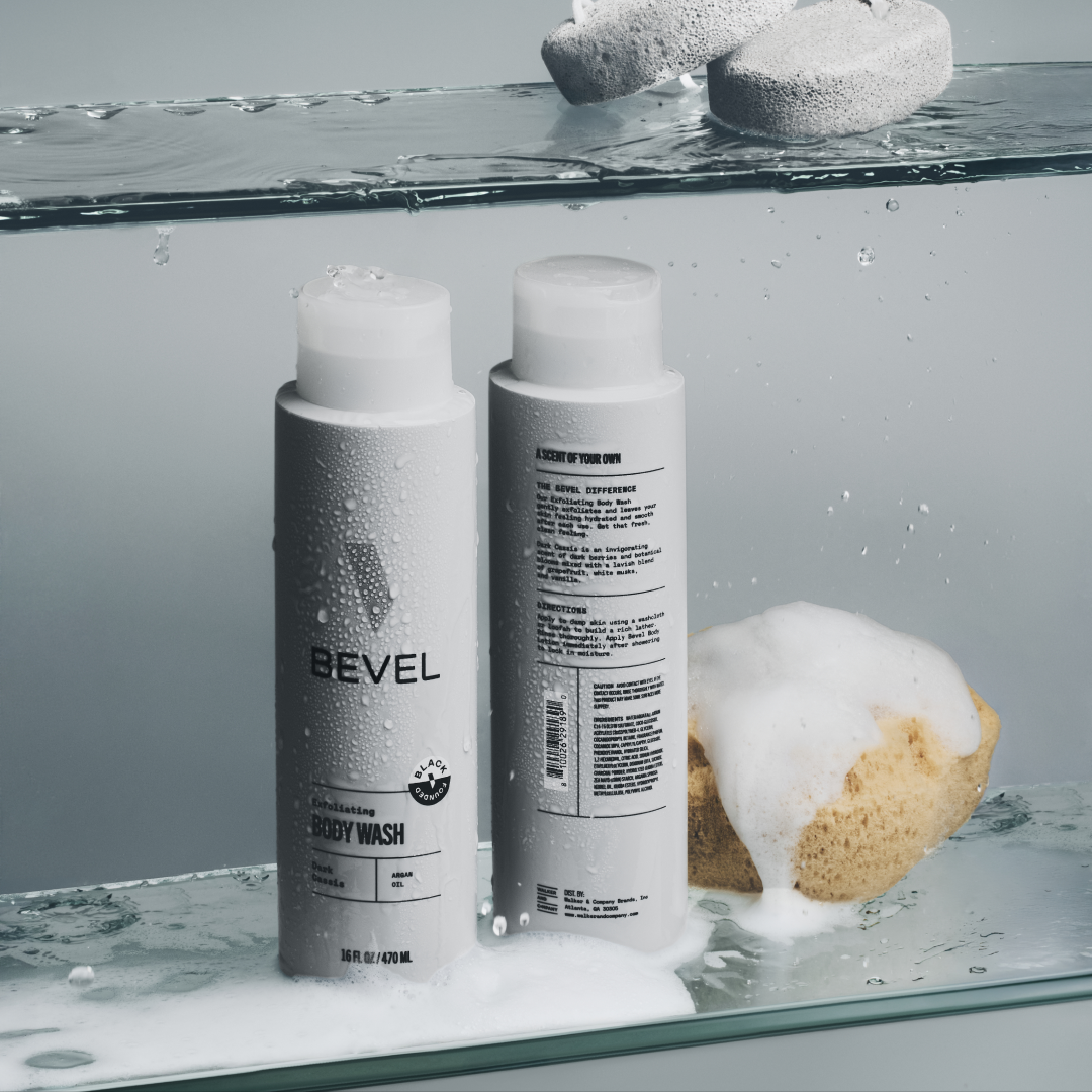 Two BEVEL body wash bottles with a sponge and soap bubbles on a glass surface.